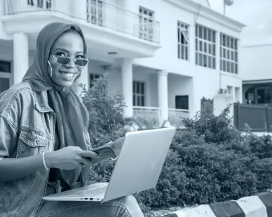 african-female-sitting-outside-with-her-laptop-phone-making-payment-online